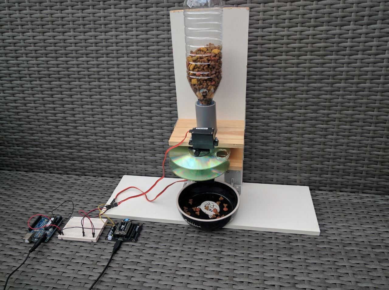 Makeshift food hopper with dispensing mechanism on top of a cat bowl. Controlled by a WiPy and Arduino through a breadboard.